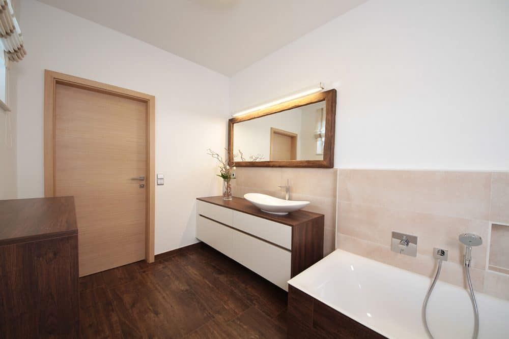 Modernes Badezimmer mit Holztür, Waschtischspiegel und weißer Badewanne auf dunklem Boden.