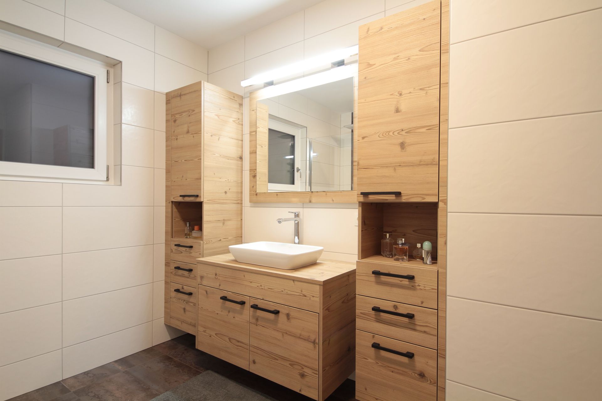 Modernes Badezimmer mit hellem Holzwaschtisch, großem Spiegel, weiß gefliesten Wänden und einem kleinen Fenster