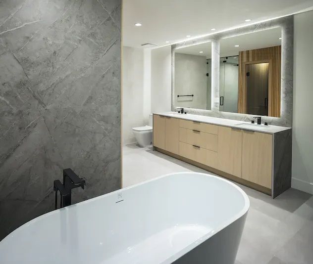 Modernes Badezimmer mit freistehender Badewanne, Doppelwaschtisch, großem Spiegel und grauer Steinwand.