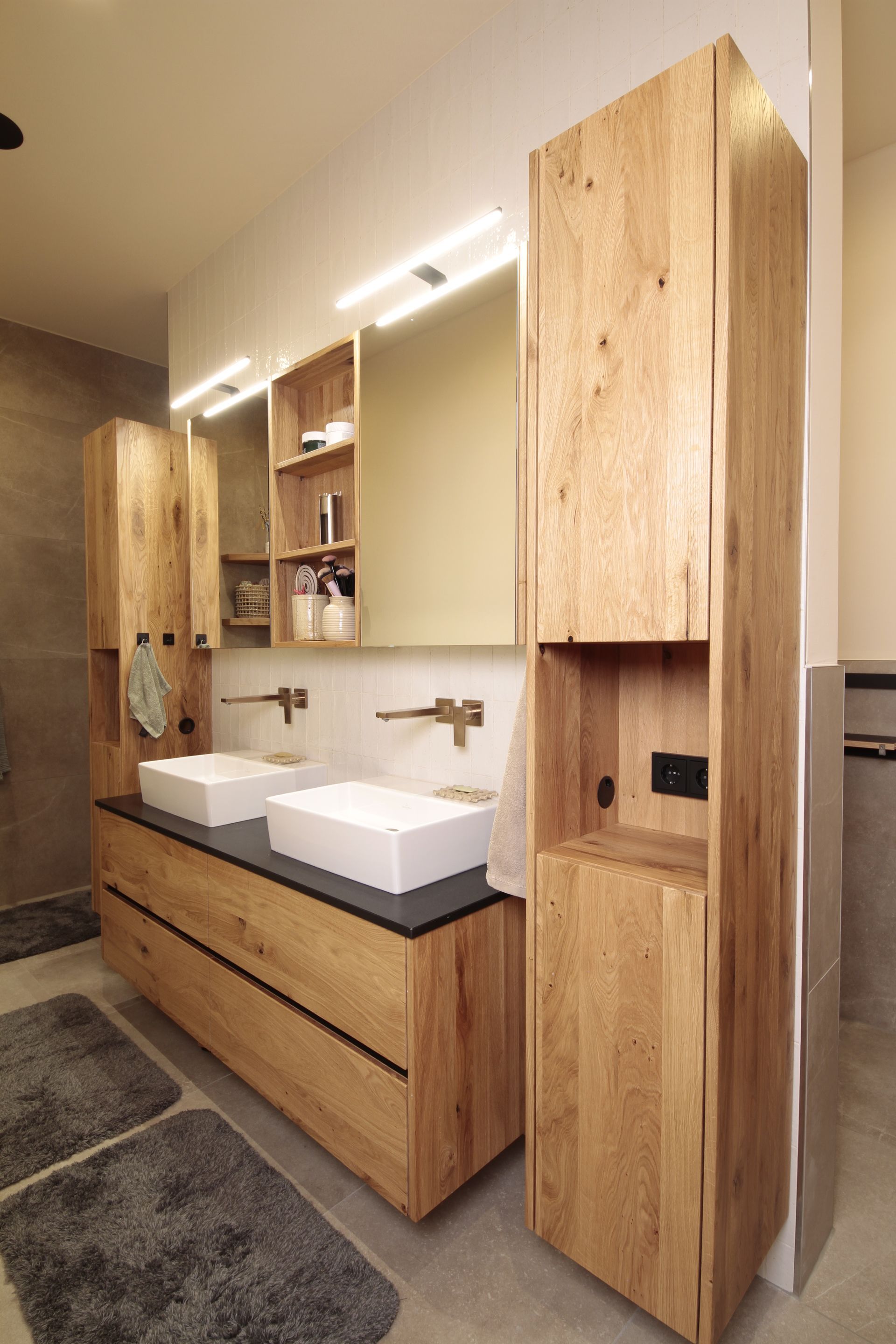Moderner Badezimmer-Waschtisch mit zwei Aufsatzwaschbecken, hellen Holzschränken und hohen Spiegelschränken.
