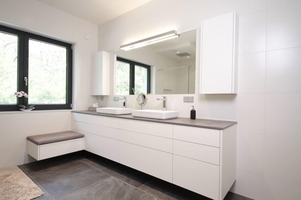 Helles, modernes Badezimmer mit weißem Doppelwaschtisch, großem Spiegel, Fenster und eingebauter Sitzbank.