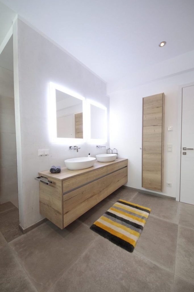 Modernes Badezimmer mit schwebendem Waschtisch aus Holz, beleuchtetem Spiegel, Waschbecken und gestreiftem Teppich