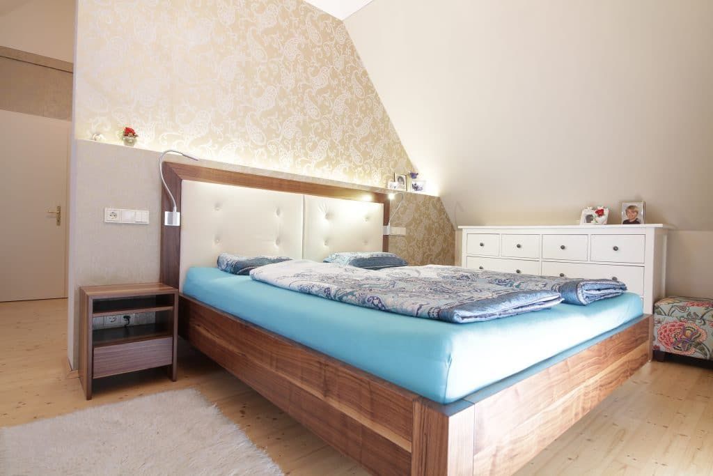 Helles Schlafzimmer mit blauer Tagesdecke, Holzbettgestell und einer weißen Kommode an der Wand.