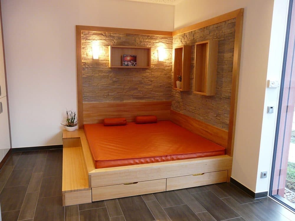 Kompakte orangefarbene Schlafnische in einem modernen Zimmer mit holzgetäfelten Wänden und eingebauten Regalen