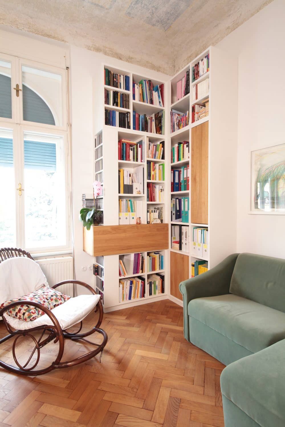 Gemütliche Wohnzimmerecke mit hohen Bücherregalen, einem grünen Sofa, einem Korbsessel und Parkettboden