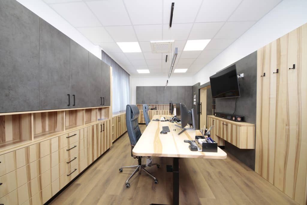 Moderner Bürokonferenzraum mit Holzschränken, blauen Stühlen, langem Tisch und an der Wand montiertem Fernseher.