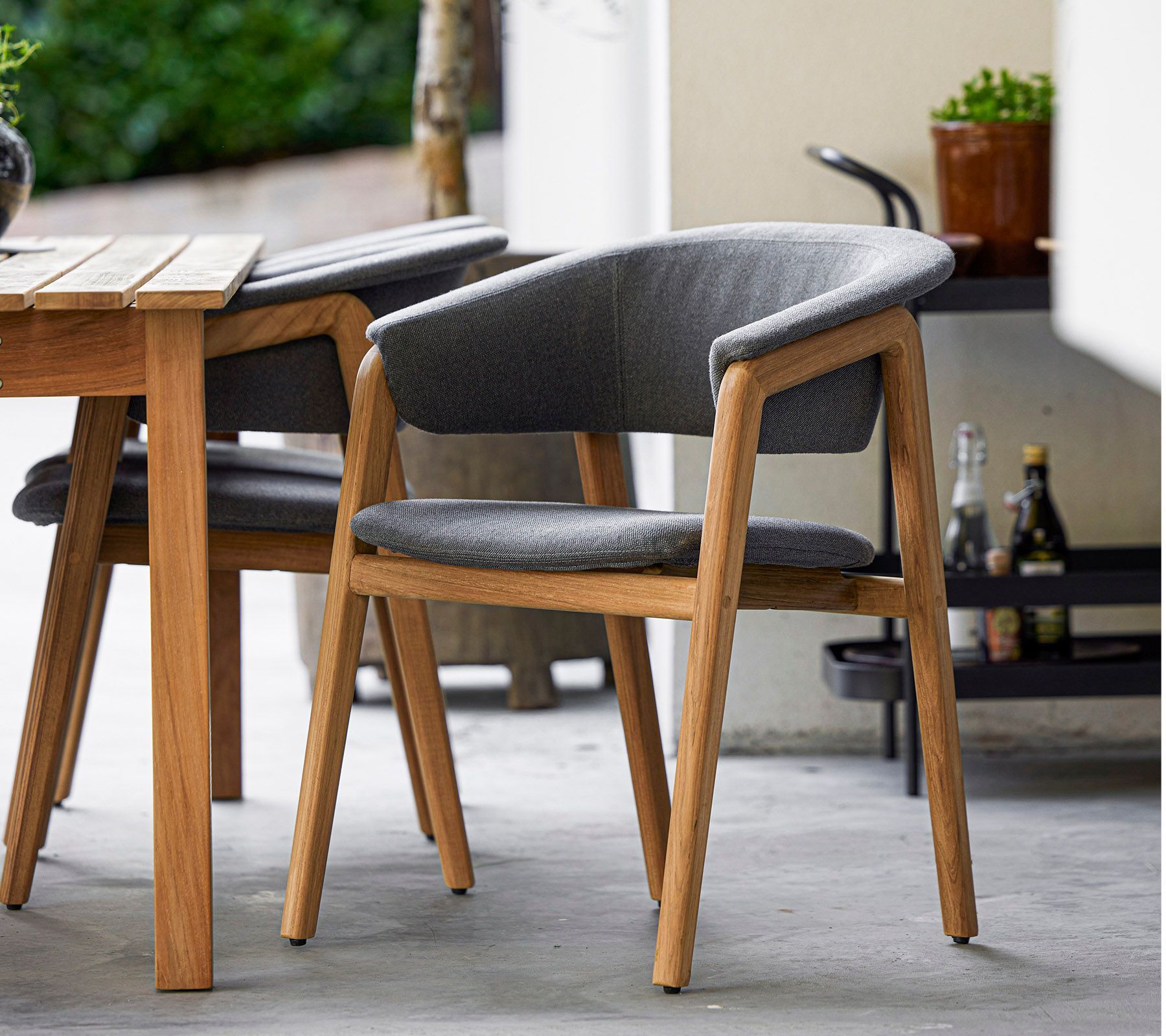 Holzesszimmerstuhl mit grauem Sitzkissen neben einem Holztisch auf einer Terrasse