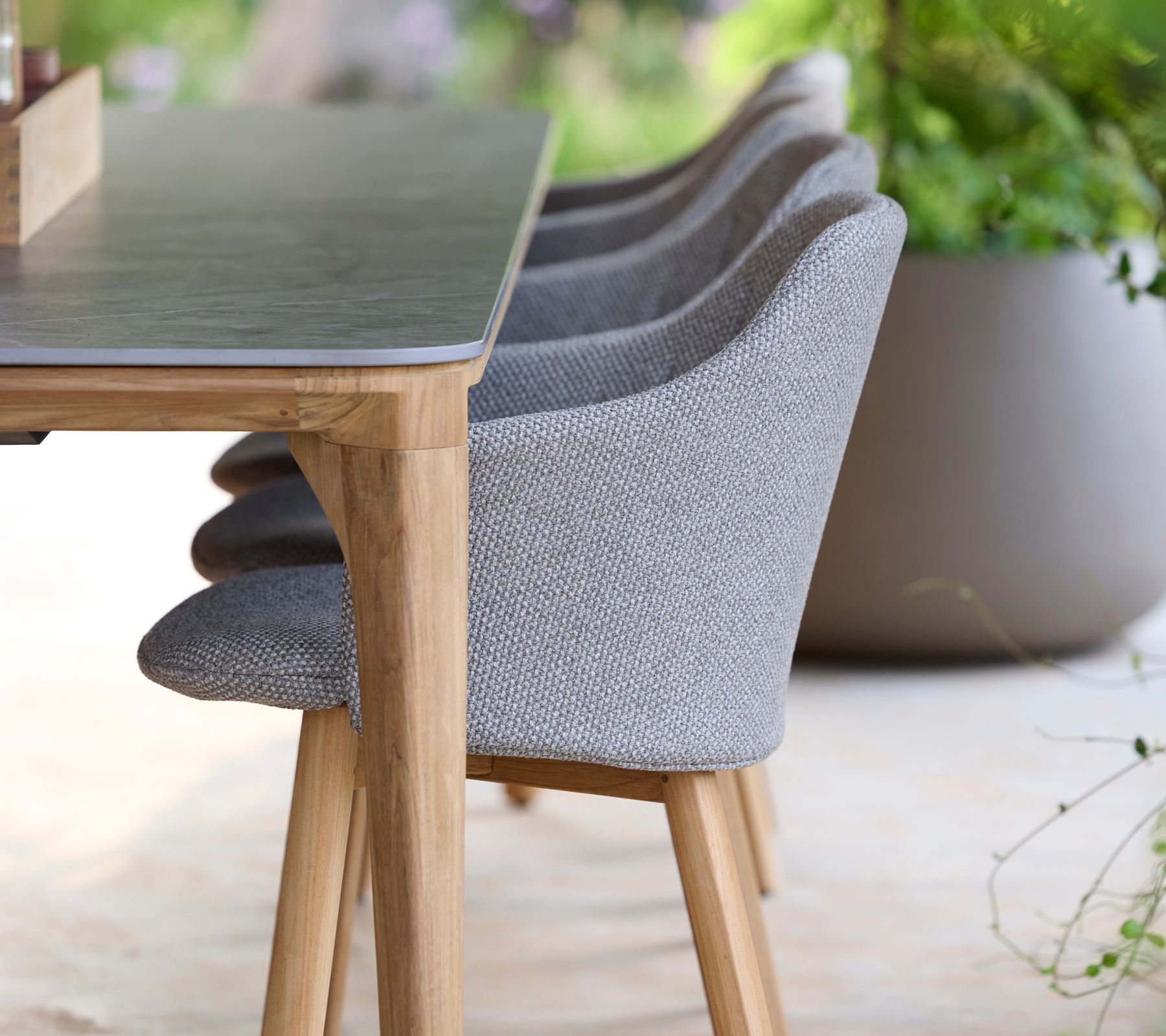 Graue Polsterstühle neben einem Holztisch auf einer hellen Terrasse