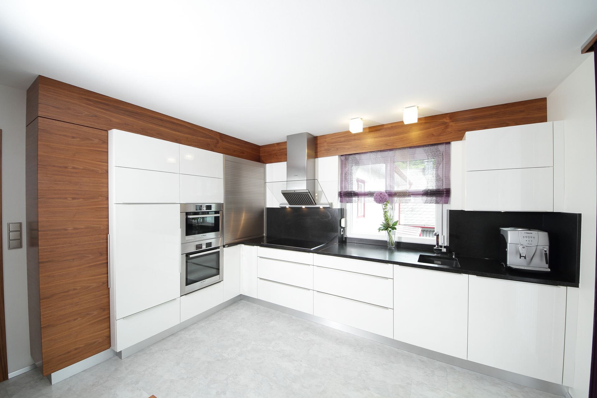 Moderne weiße Küche mit schwarzen Arbeitsplatten, einer Akzentwand aus Backstein, einem eingebauten Backofen 
