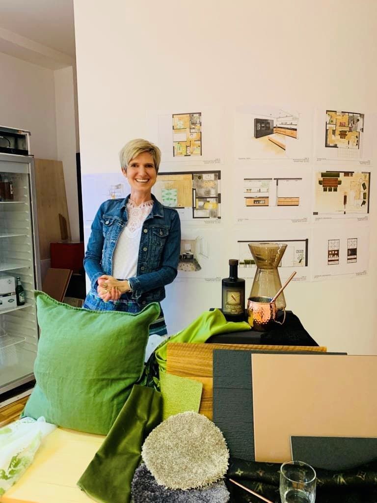 Eine Person steht in einem Ausstellungsraum, Präsentationstischen und an der Wand befestigten Designmustern.