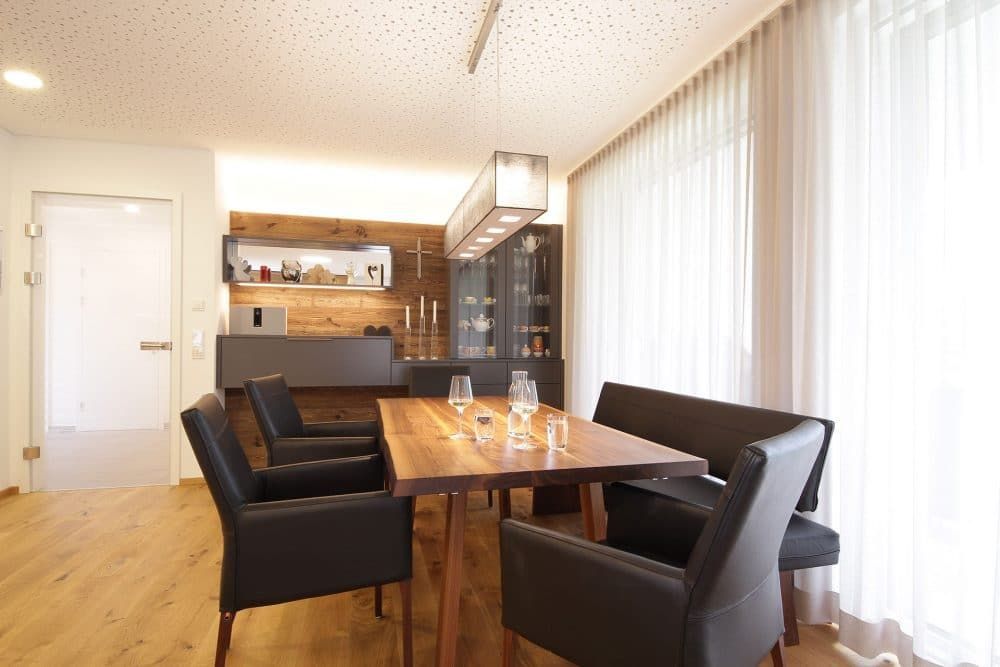 Modernes Esszimmer mit Holztisch, schwarzen Stühlen und großen Fenstern mit transparenten Vorhängen.
