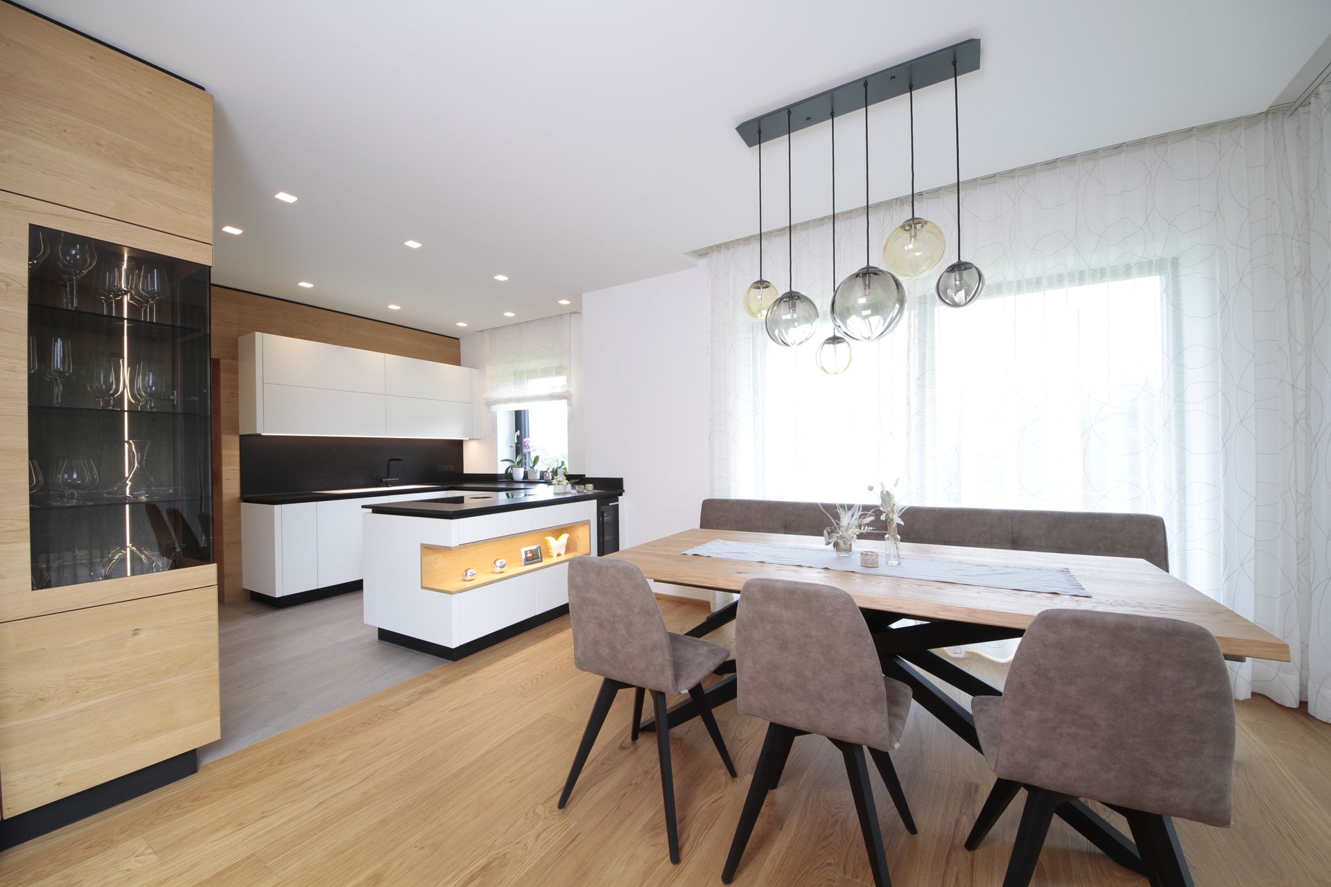 Moderne, offene Küche mit Essbereich, Holztisch, Pendelleuchten und hellen Fenstern