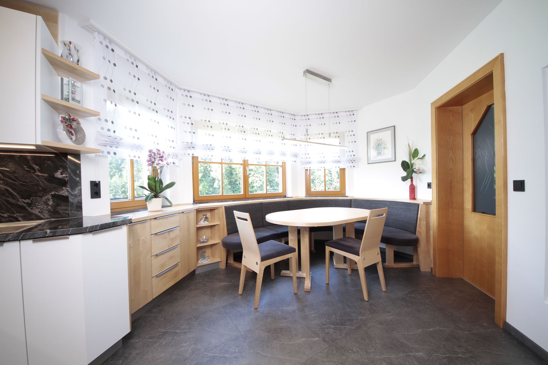 Helle Wohnküche mit Holztisch, Stühlen, weißen Schränken und großen Fenstern