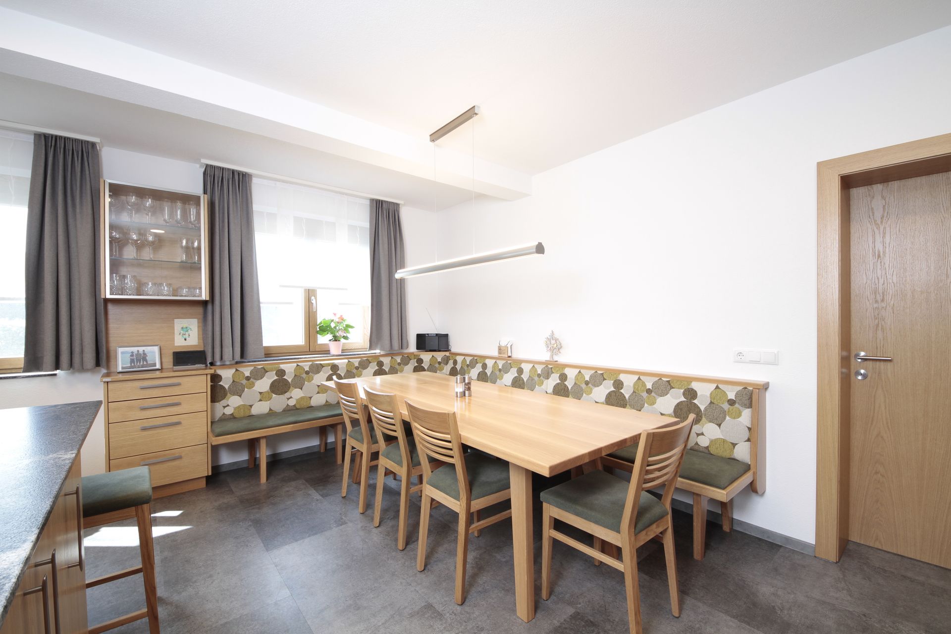 Helles Esszimmer mit Holztisch, Stühlen, Sitzbank, Fenster und grauem Fliesenboden