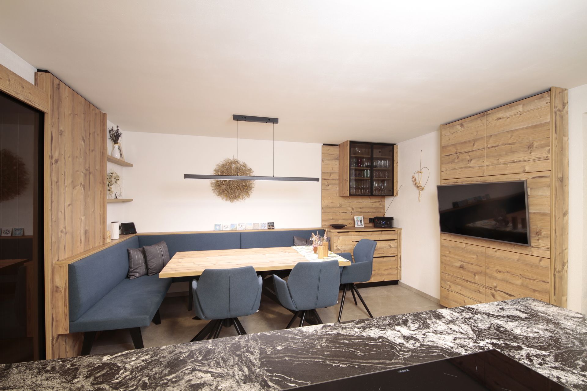 Modernes Wohn-Esszimmer mit blauen Stühlen, Holzelementen, an der Wand montiertem Fernseher und einem langen Tisch 