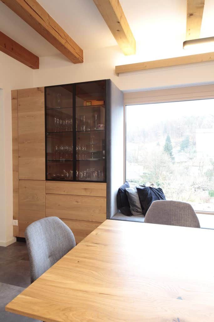 Modernes Esszimmer mit Holztisch, grauen Stühlen und einem großen Fenster mit Blick auf Bäume und Berge