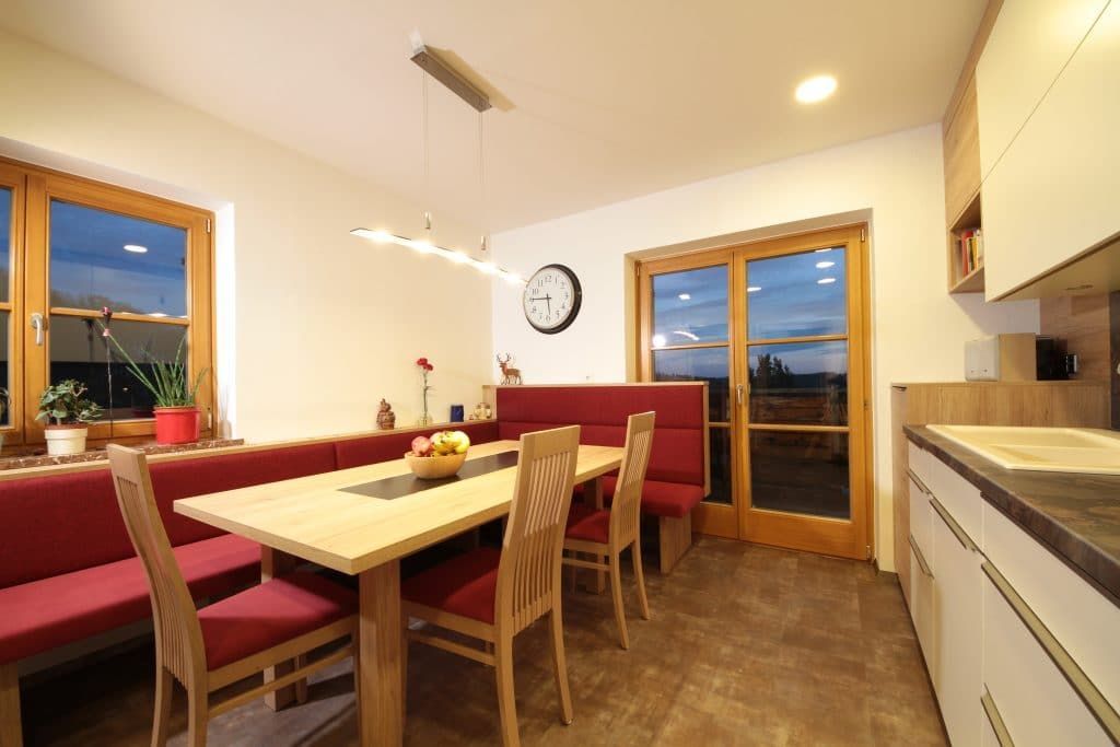 Helles Esszimmer mit roten Stühlen, Holztisch und großen Fenstern in der Abenddämmerung