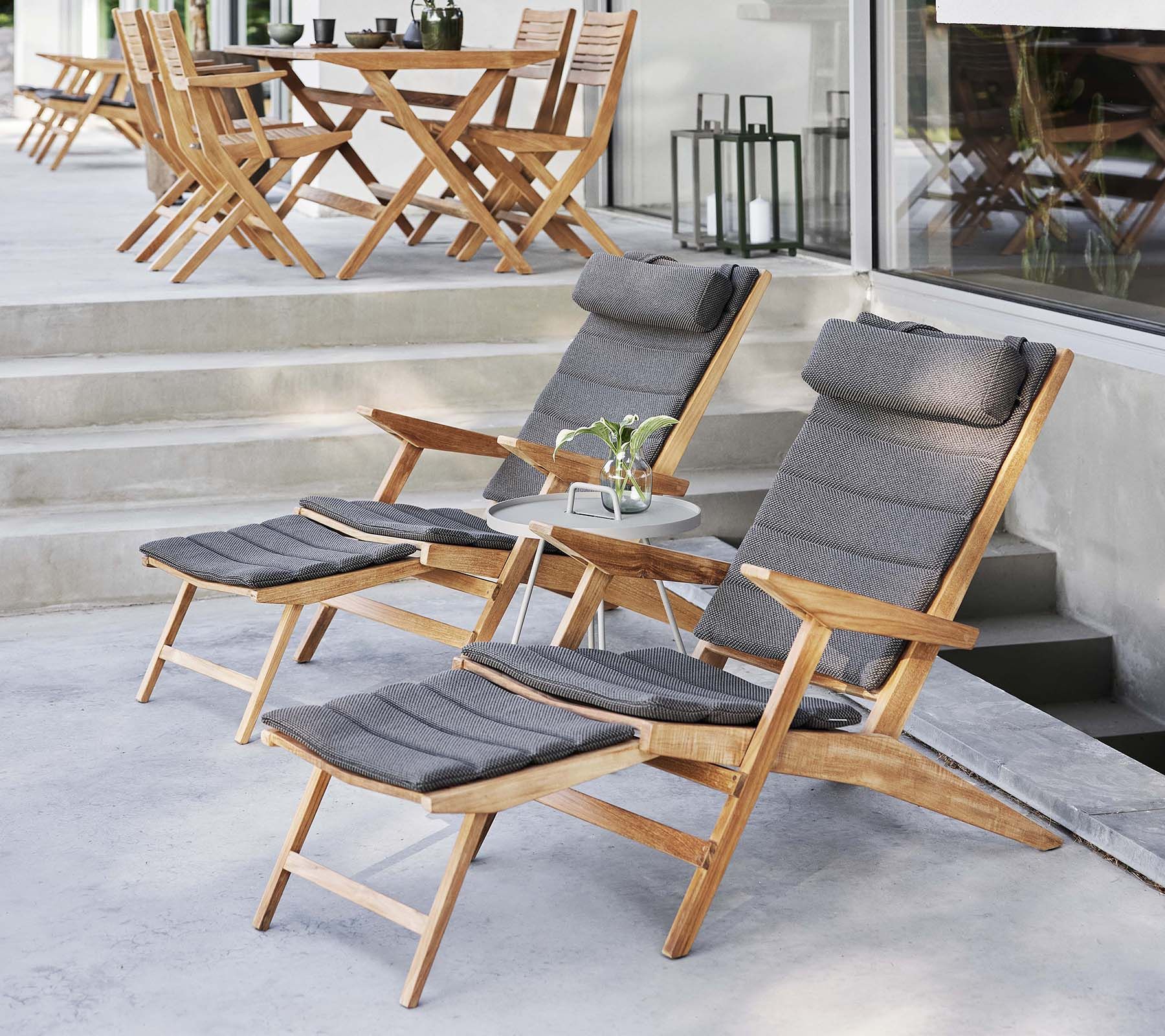 Holzliegen mit grauen Kissen und ein kleiner Tisch auf einer sonnigen Terrasse