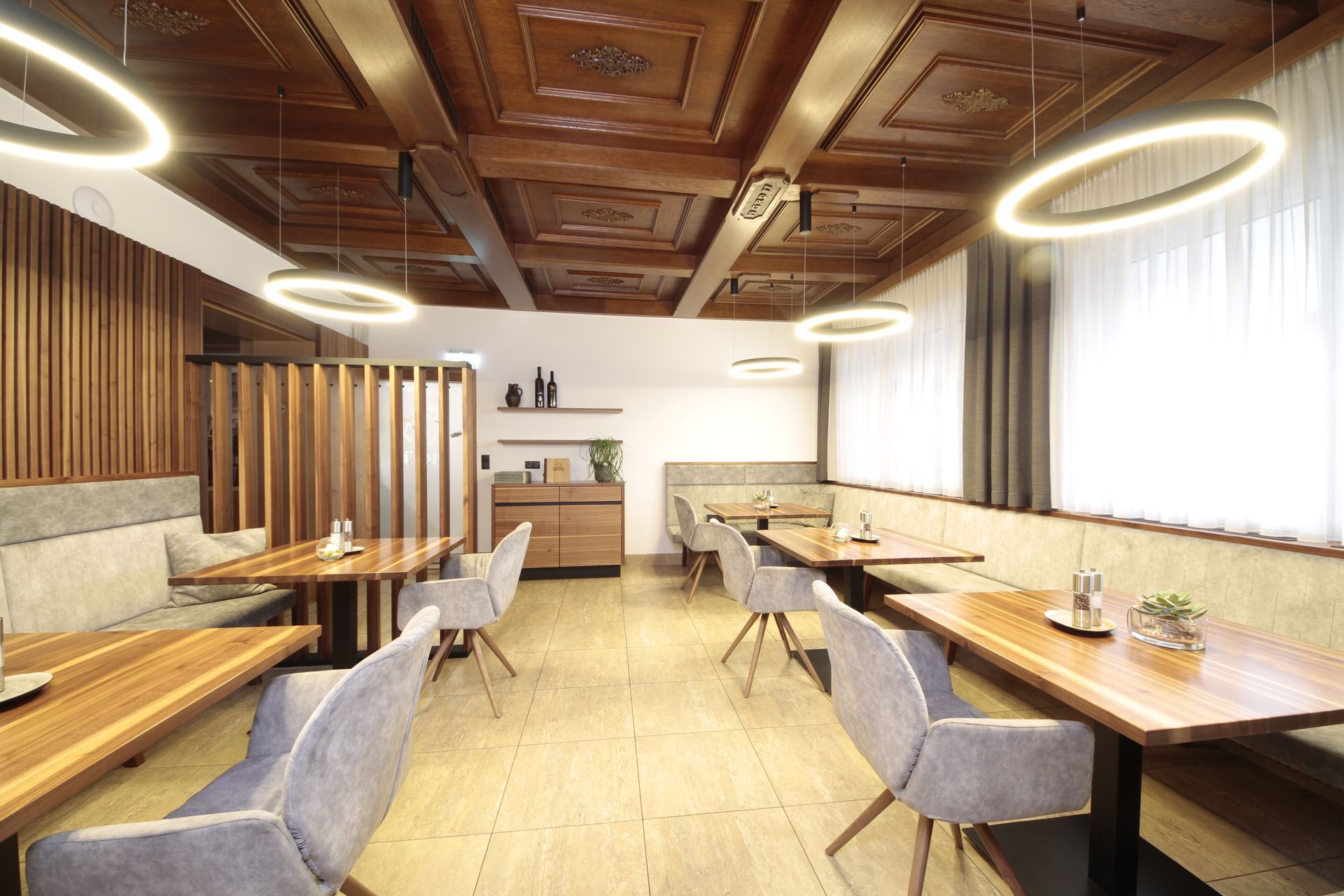Modernes Café-Interieur mit Holzdecke, langen Tischen und grauen Stühlen an großen Fenstern