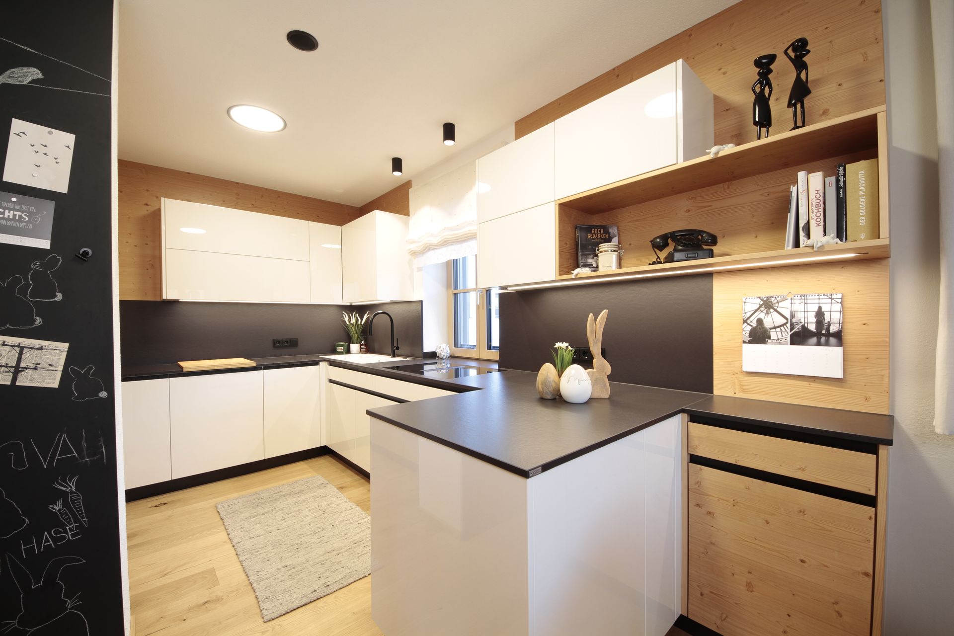 Moderne Küche mit weißen Schränken, schwarzen Arbeitsplatten, Holzregalen und einer kleinen Kochinsel.