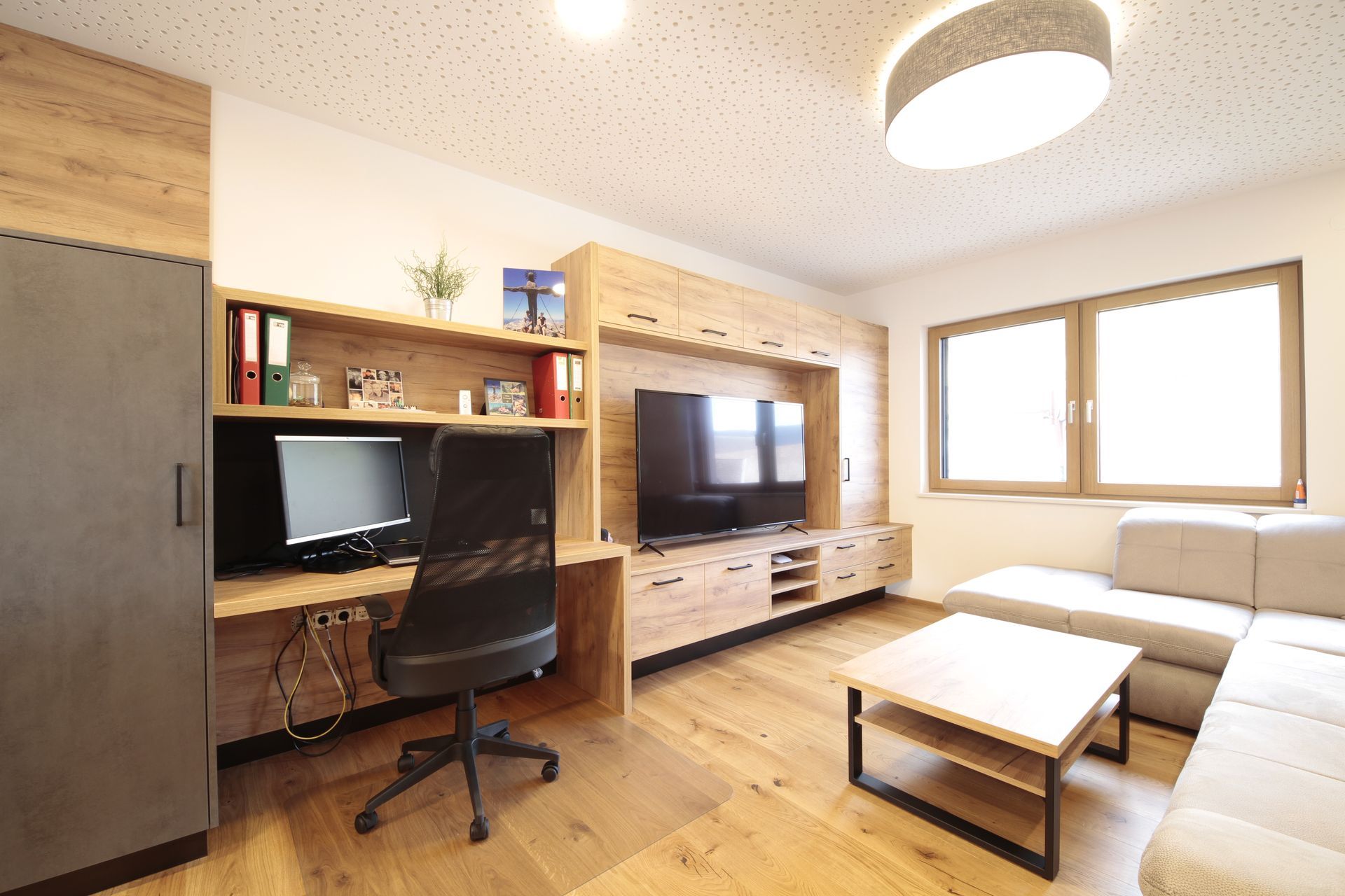 Modernes Wohnzimmer mit Schreibtisch, Fernseher, beigefarbenem Sofa, Couchtisch und großen Fenstern