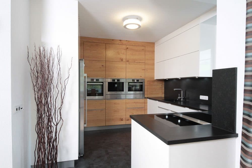 Moderne Küche mit Holzschränken, schwarzen Arbeitsplatten und weißen Schränken auf der rechten Seite.