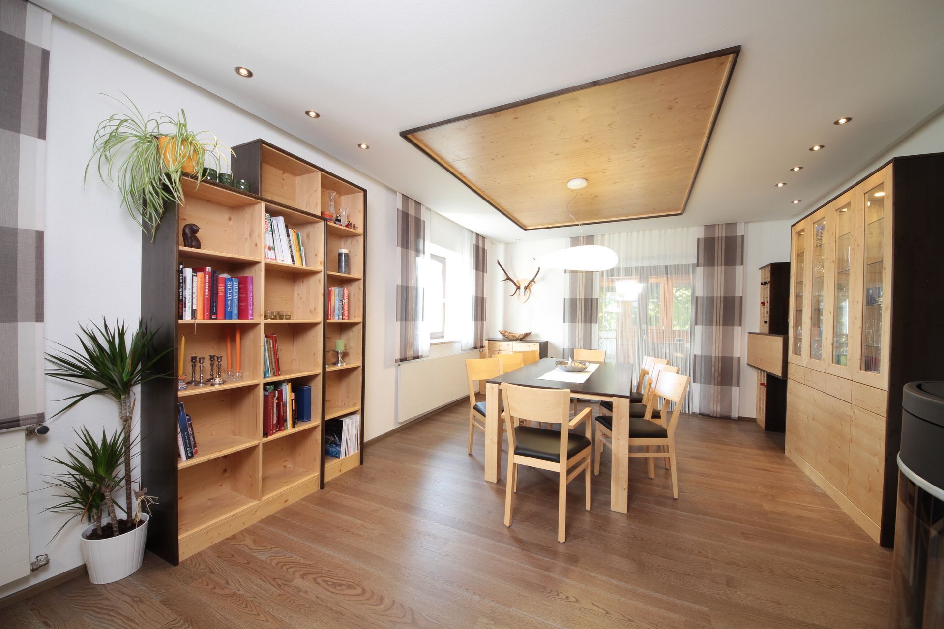 Modernes Esszimmer mit Holztisch, Stühlen, Bücherregalen, Pflanzen und warmem Einbaulicht