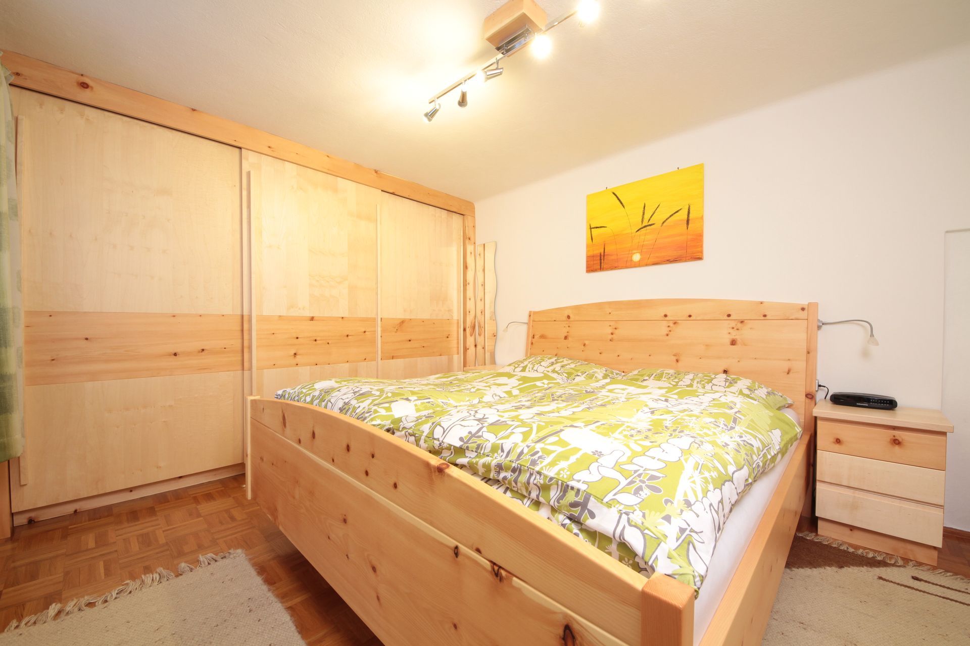 Helles Schlafzimmer mit Holzbett, Kleiderschrank, Nachttisch und gelber Bettwäsche mit Blumenmuster.