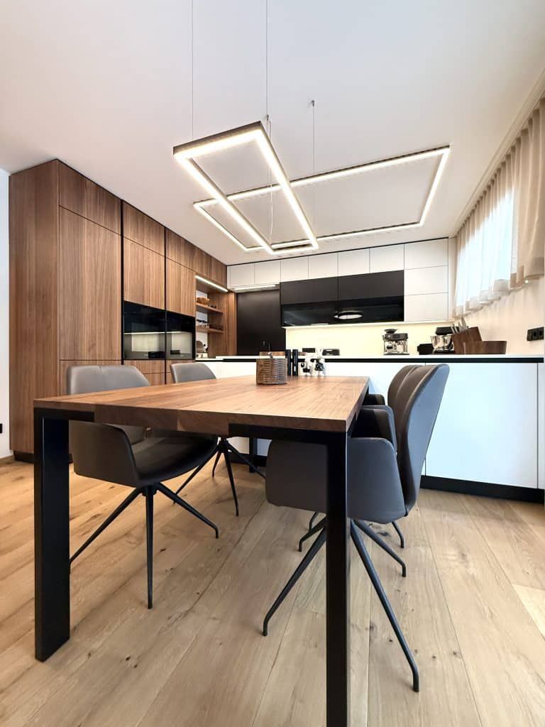 Moderne Küche und Essbereich mit Holztisch, schwarzen Stühlen und großen Fenstern mit Jalousien.