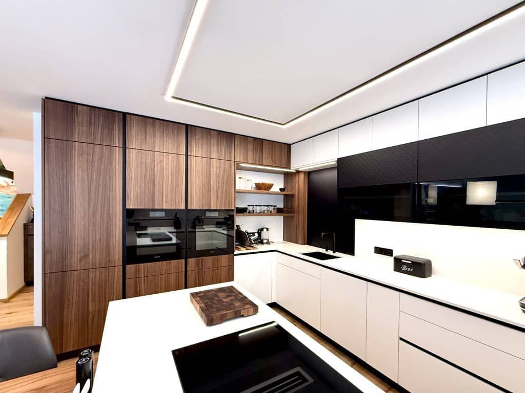Moderne Küche in Weiß und Holz mit schwarzen Einbaugeräten und Hochglanzschränken