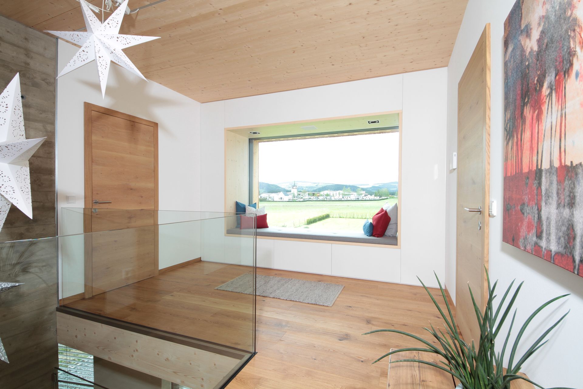 Moderner Flur mit Holzboden, Glasgeländer, Sternendekorationen und einer großen Fensterbank mit Blick auf eine Landschaft