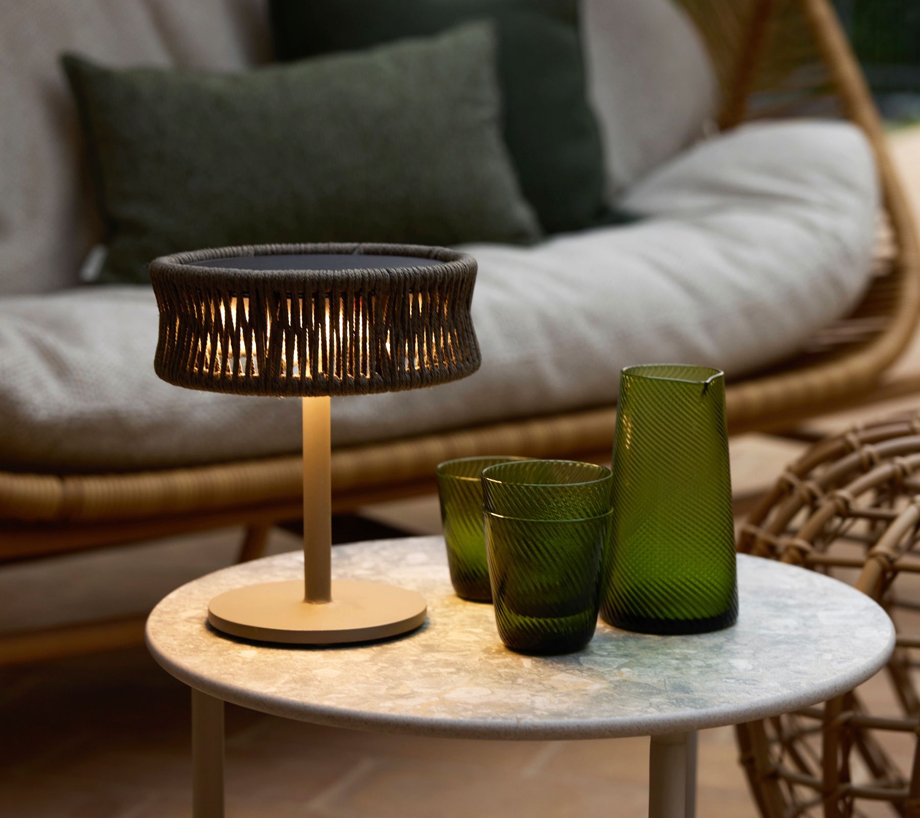 Moderner Terrassentisch mit schwarzer Lampe und grünen Gläsern in einer gemütlichen Outdoor-Lounge