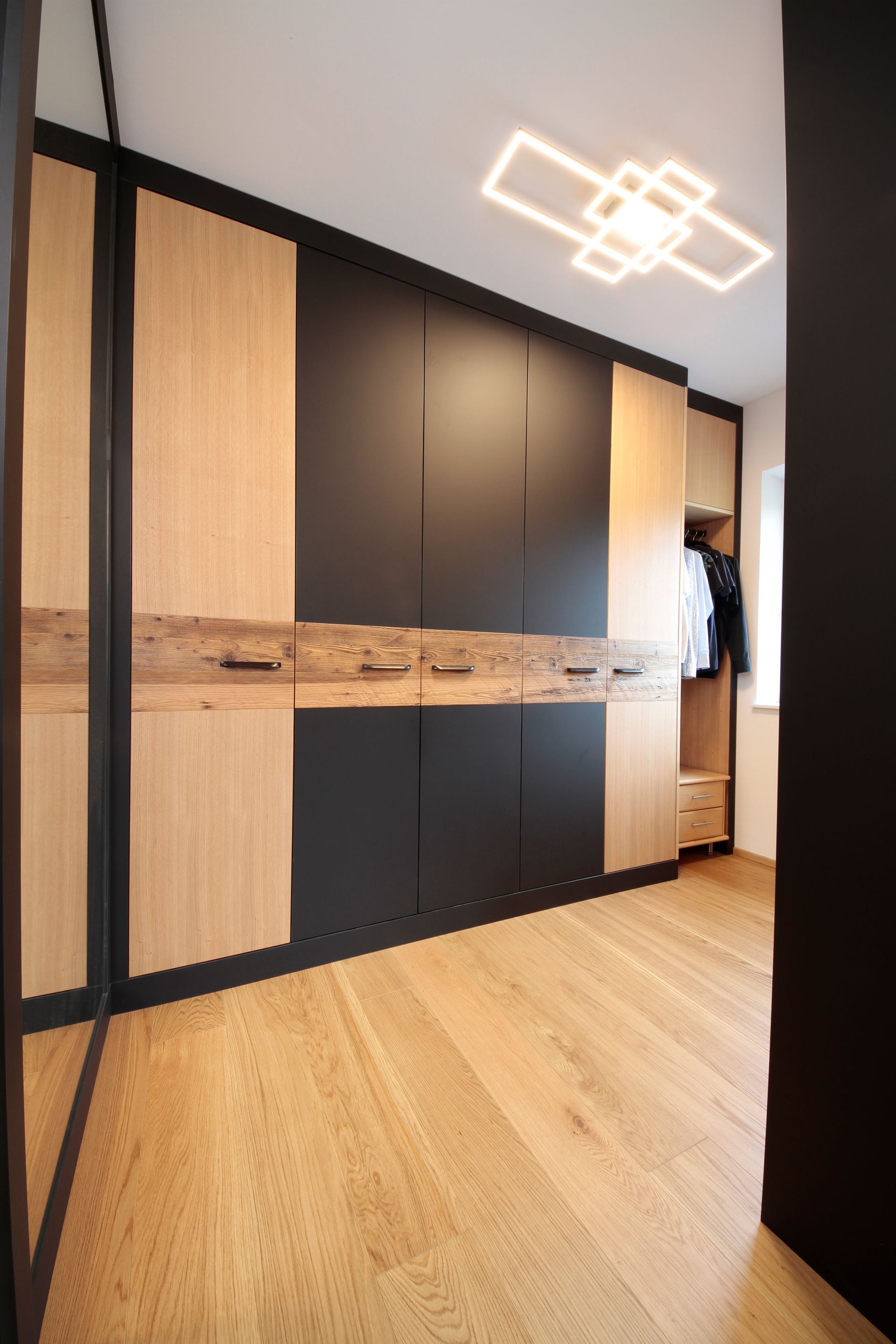 Moderner Flur mit schwarzen und hölzernen Einbauschränken, hellem Holzboden und geometrischer Deckenleuchte