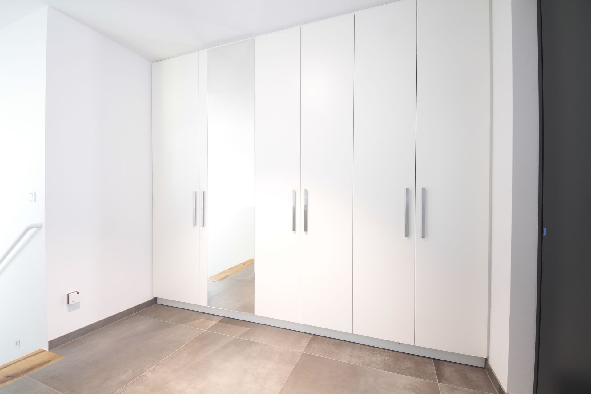 Weiße Einbauschränke in einem hellen, leeren Zimmer mit beigefarbenem Fliesenboden