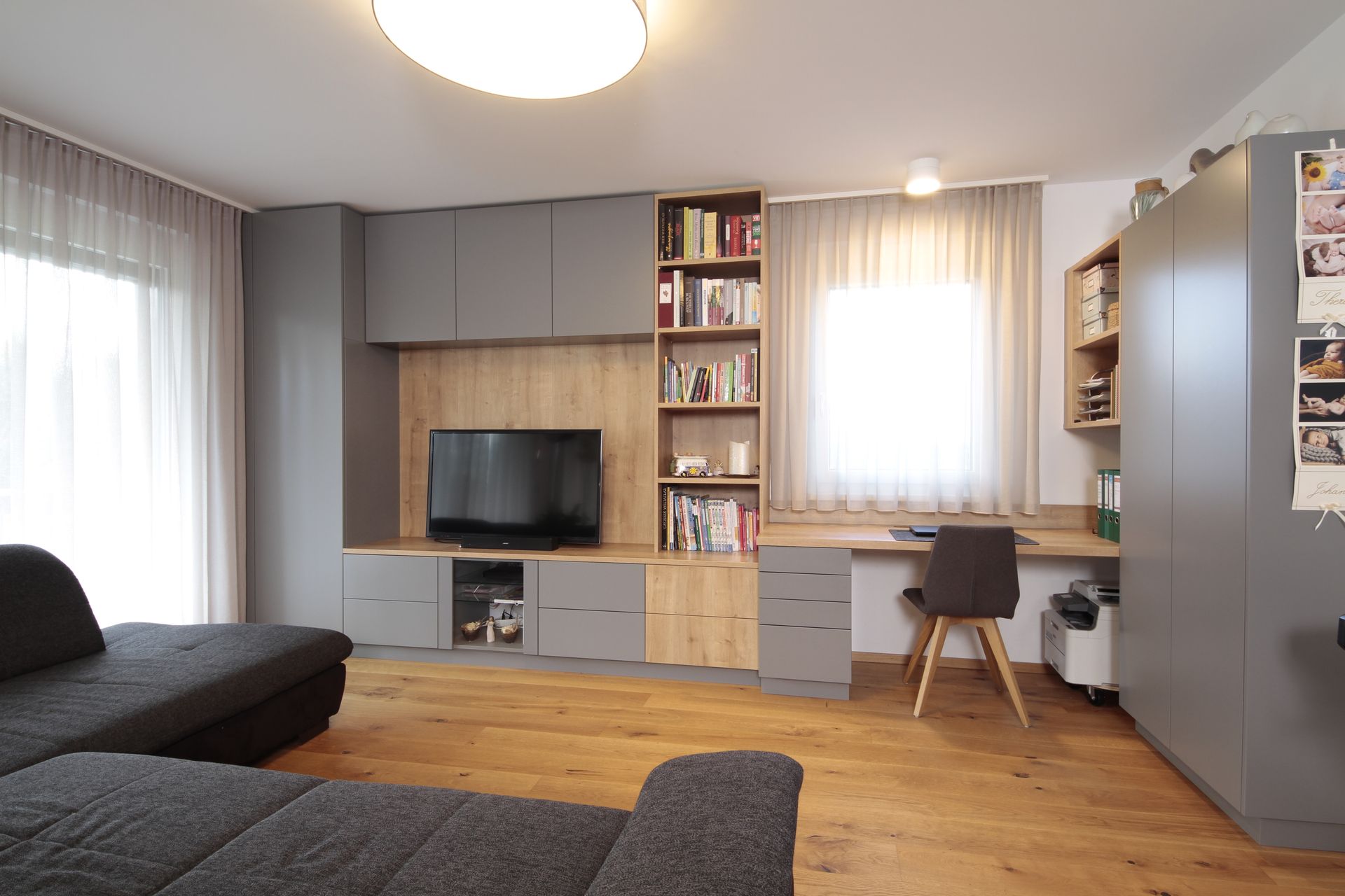 Modernes Wohnzimmer mit grauem Sofa, TV-Möbel, Holzboden und Schreibtisch am Fenster