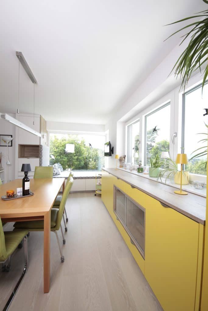 Helle, moderne Küche mit gelben Schränken, Holztisch und großen Fenstern mit Blick ins Grüne