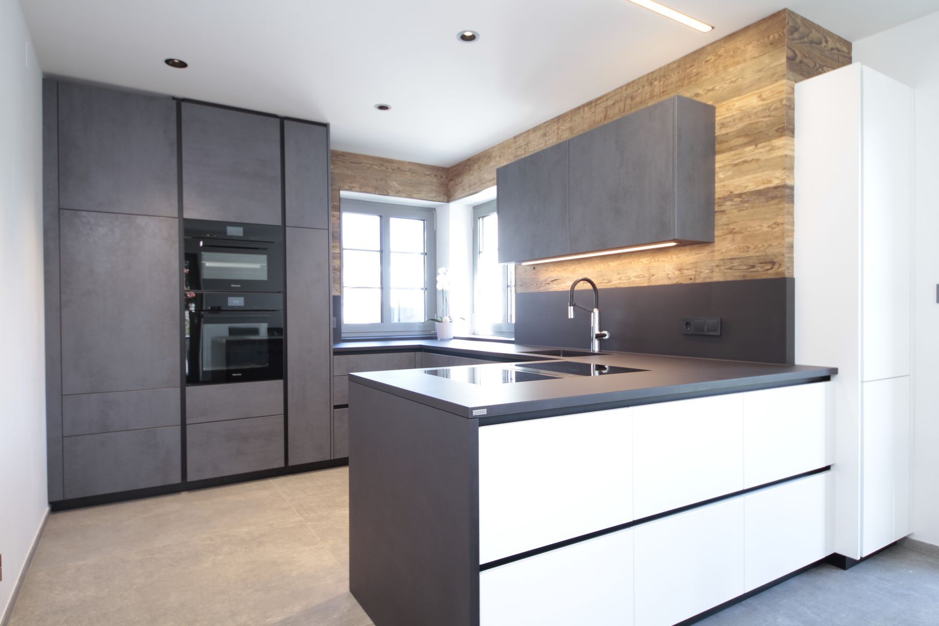 Moderne Küche mit dunklen Schränken, weißer Kochinsel, Einbaubackofen und großem Fenster