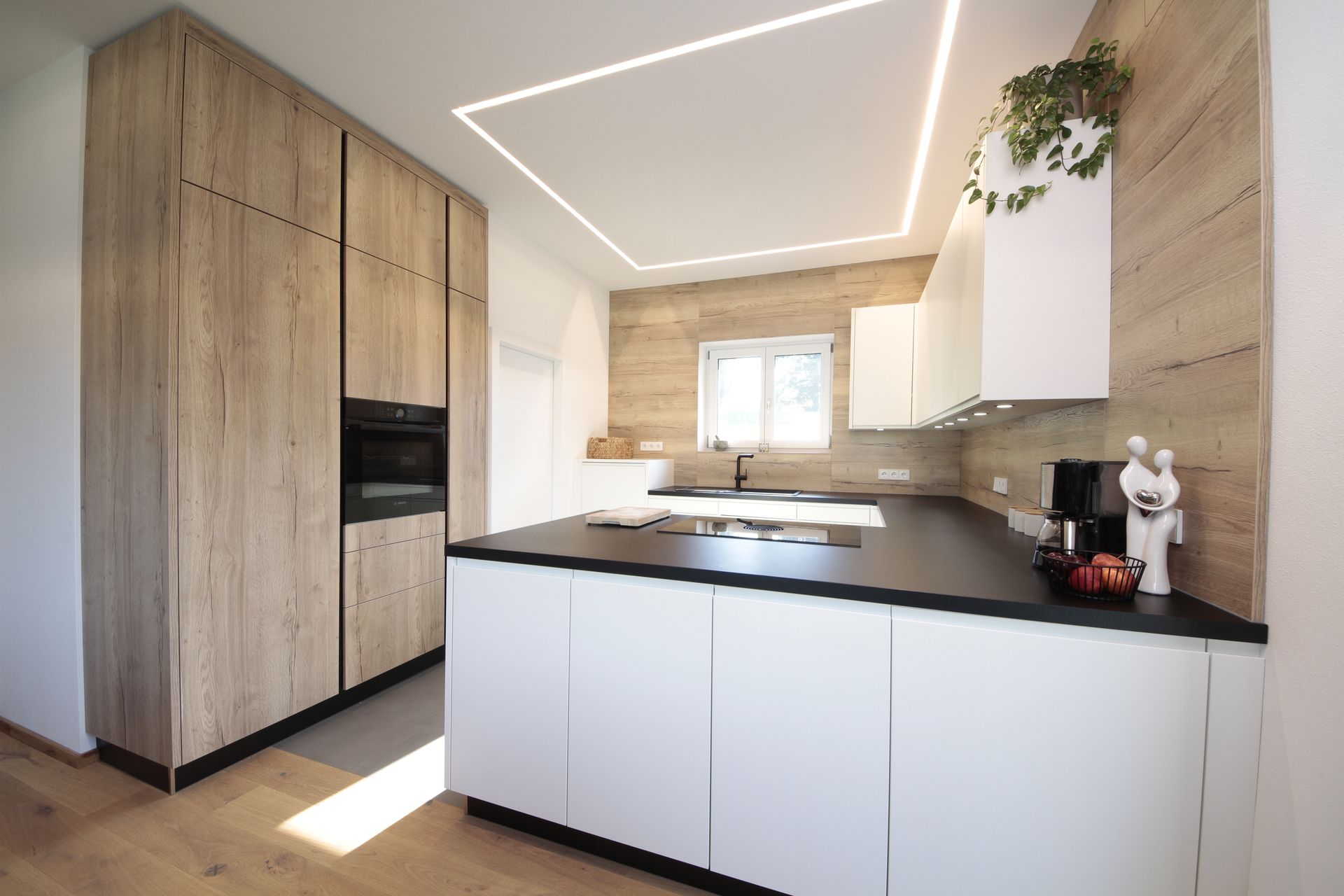 Moderne Küche mit weißen Schränken, schwarzen Arbeitsplatten, Holzelementen und Deckenbeleuchtung.
