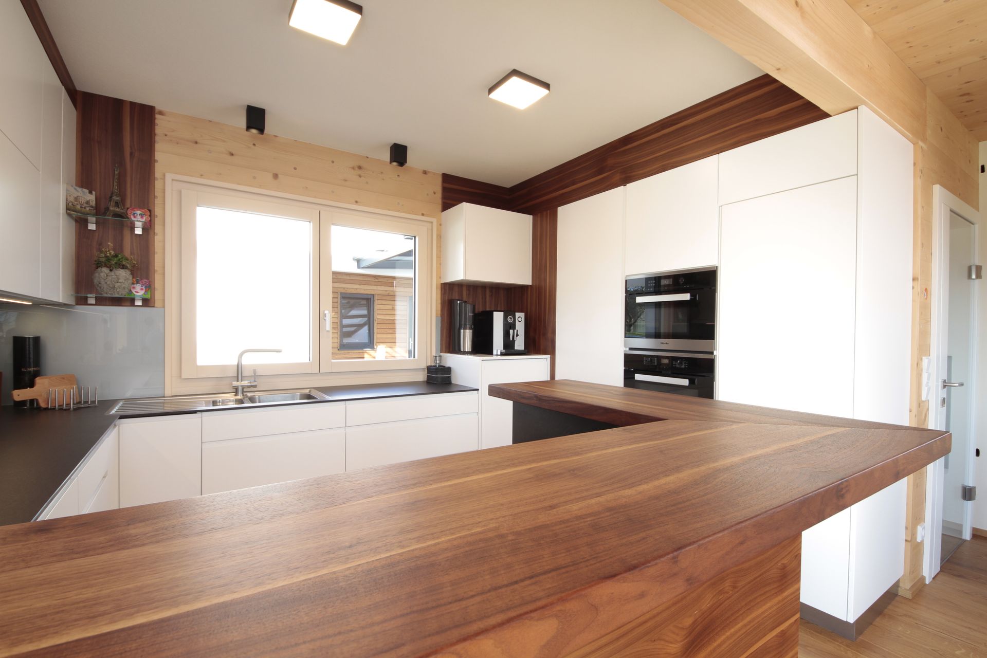 Helle, moderne Küche mit weißen Schränken, Arbeitsplatten aus Holz und großem Fenster.
