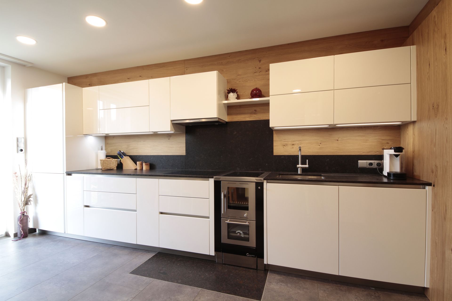 Moderne Küche mit weißen Schränken, schwarzem Fliesenspiegel und Edelstahlbackofen unter warmem Licht