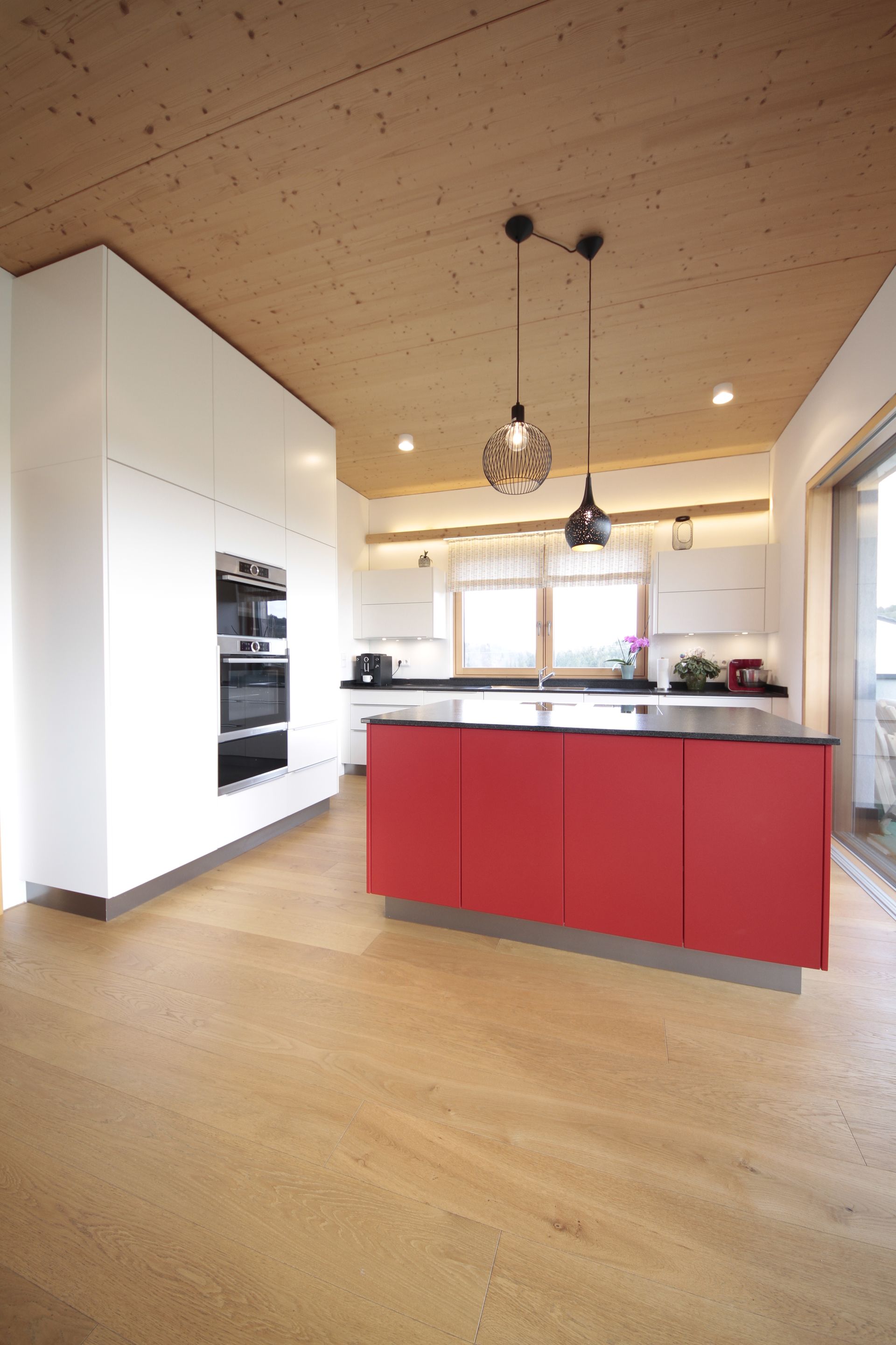 Moderne Küche mit roter Kochinsel, heller Holzdecke und großem Fenster