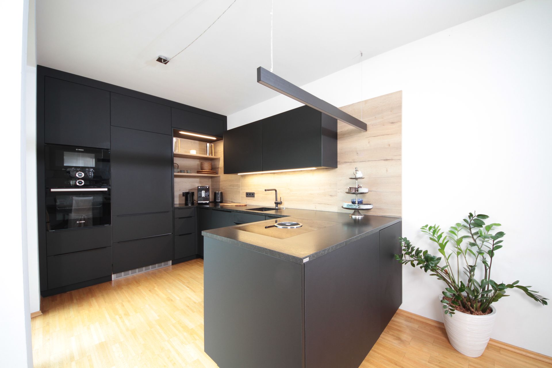 Moderne schwarz-weiße Küche mit Kochinsel, Holzboden und Topfpflanze an der Wand