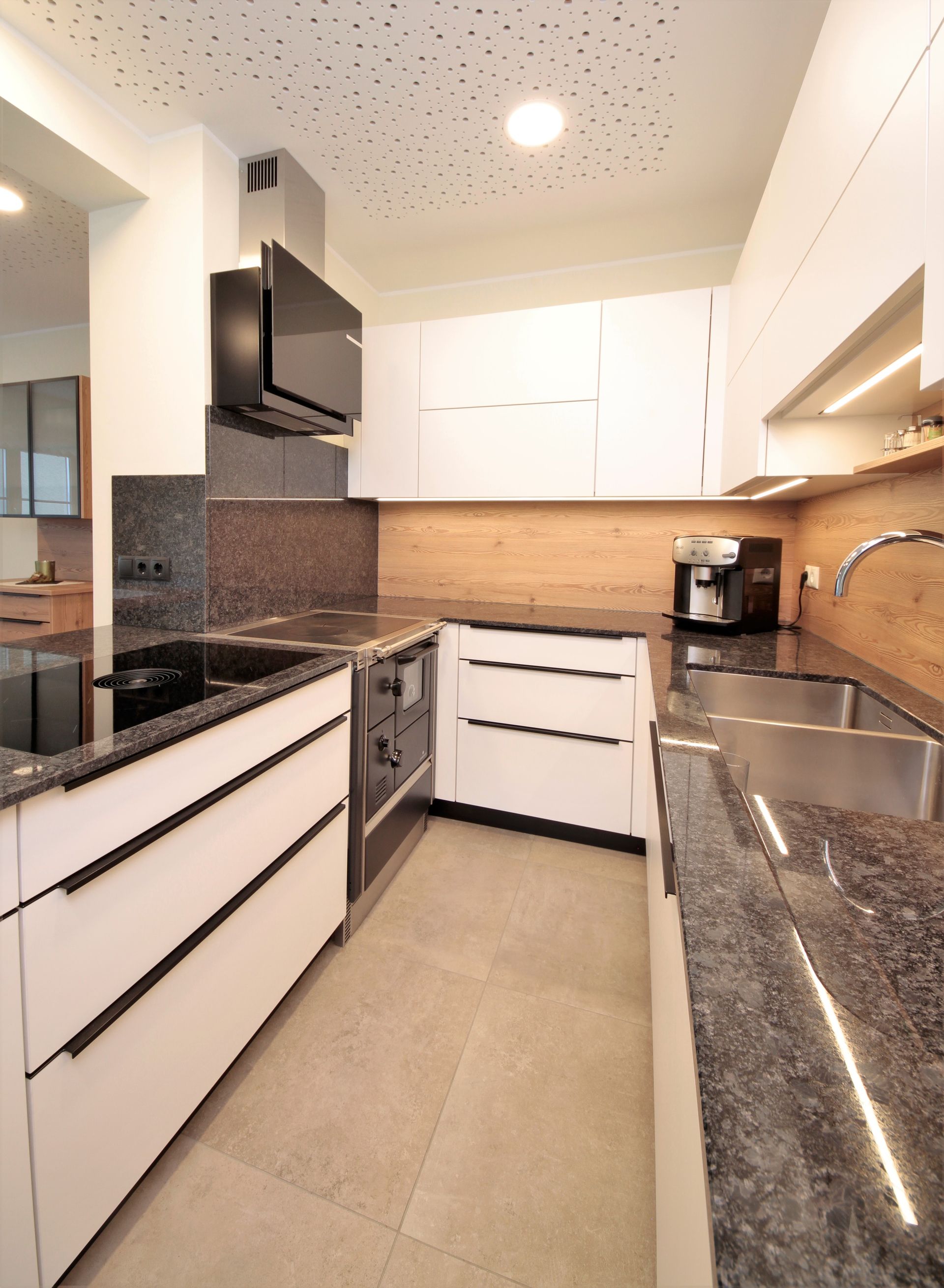 Moderne weiße Küche mit Granitarbeitsplatten, Einbaubackofen und braunem Fliesenspiegel
