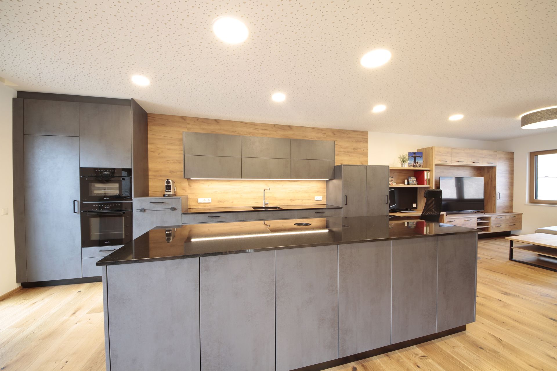 Moderne Küche mit grauer Kochinsel, Holzelementen, Einbaubacköfen und heller Einbaubeleuchtung