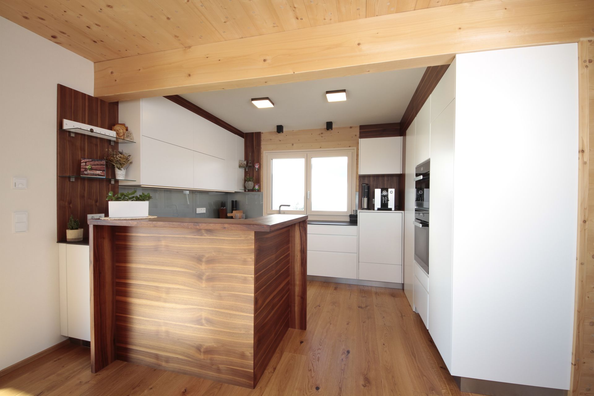 Moderne Kücheneinrichtung mit Holzdecke, Kochinsel, weißen Schränken und hellem Fensterlicht