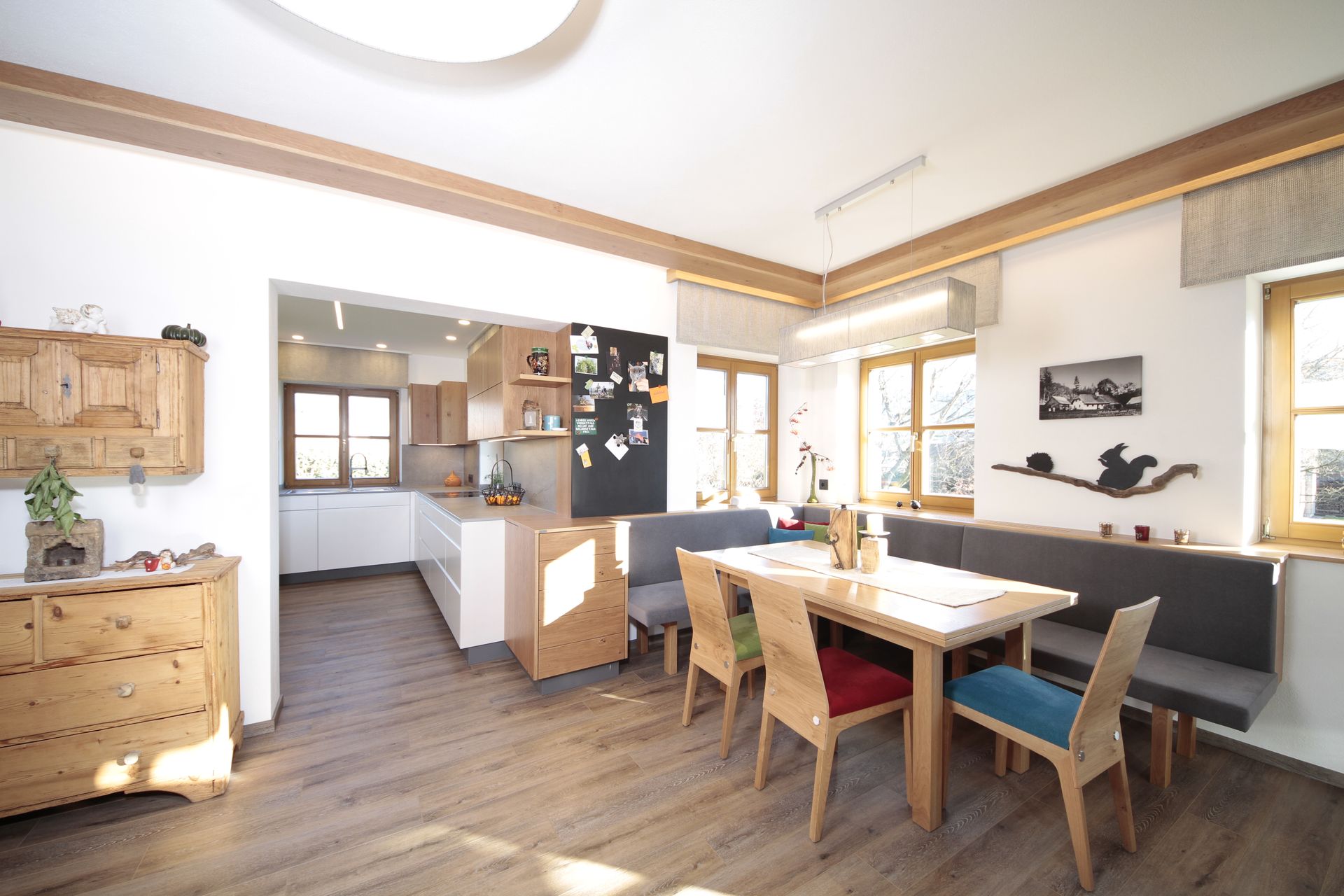 Helles Esszimmer mit Holztisch, Stühlen, Anrichte und offener Küche im Hintergrund