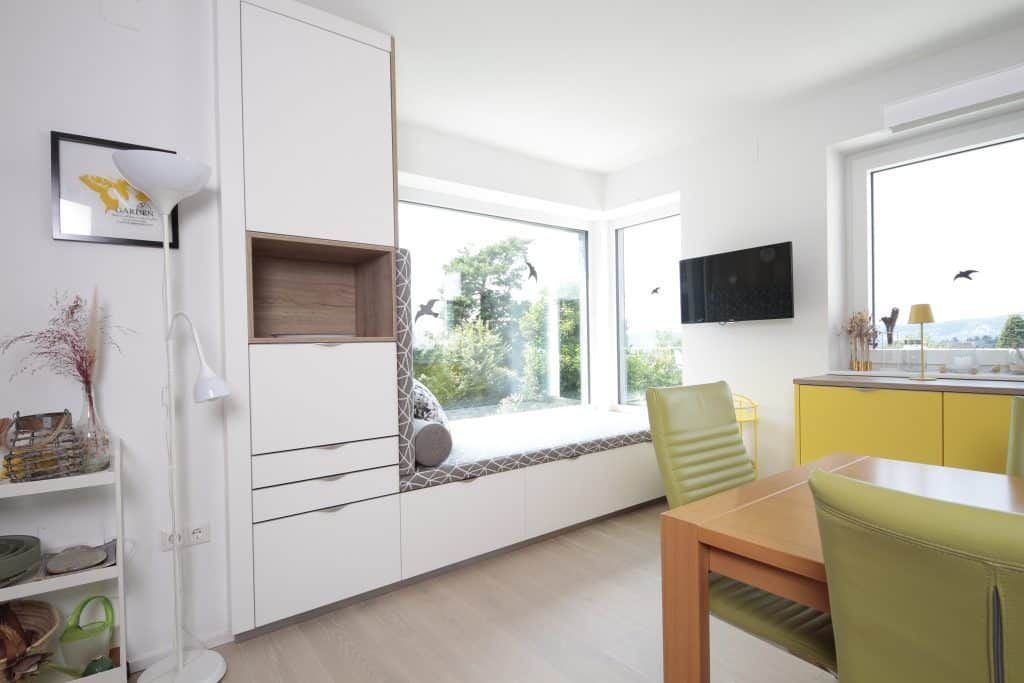 Helle, moderne Küche mit weißen Schränken, gelben Stühlen und einer großen Fenstersitznische