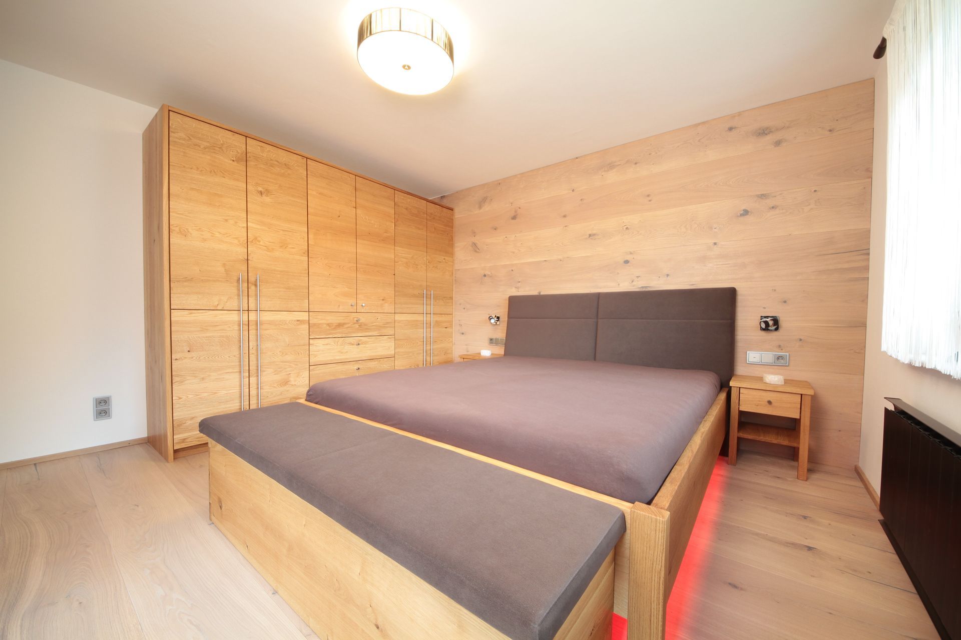 Modernes Schlafzimmer mit großem Bett, Holzschrank und hellem Holzboden.