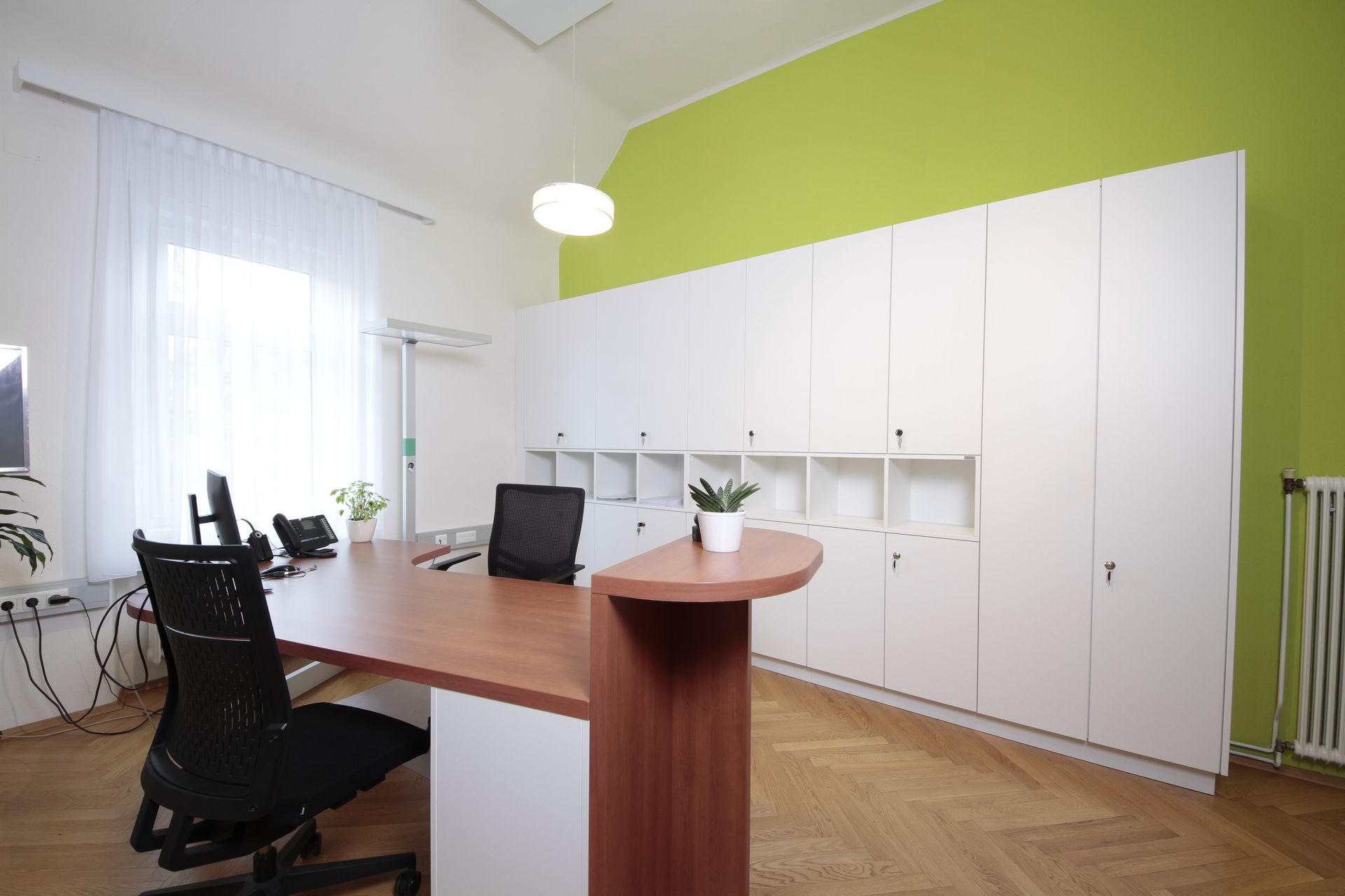 Modernes Büro mit weißen Schränken, Holzschreibtisch, schwarzen Stühlen und limettengrüner Akzentwand.