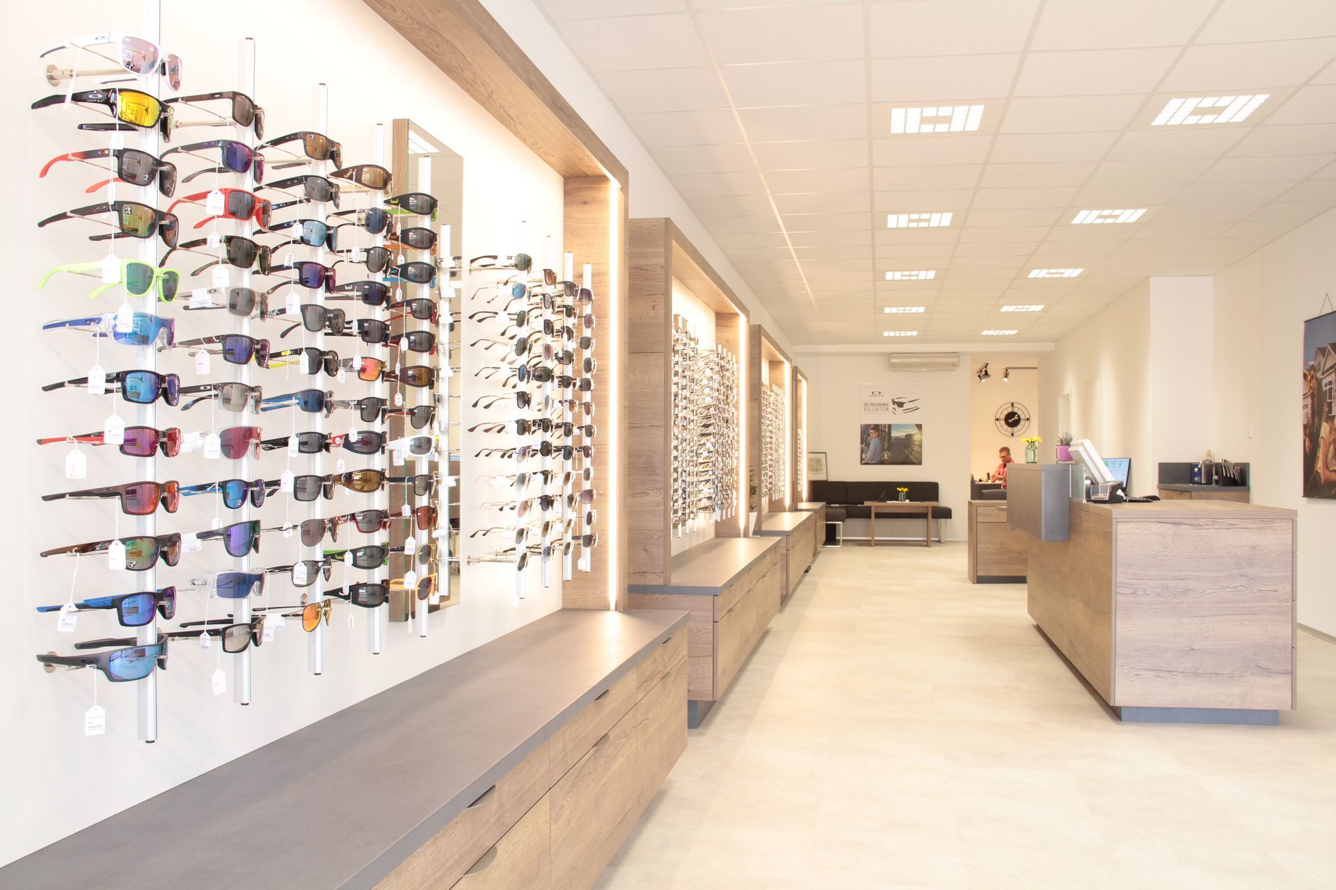 Helles Interieur eines Optikergeschäfts mit Reihen von Brillen, die an Wandständern und auf Theken ausgestellt sind.